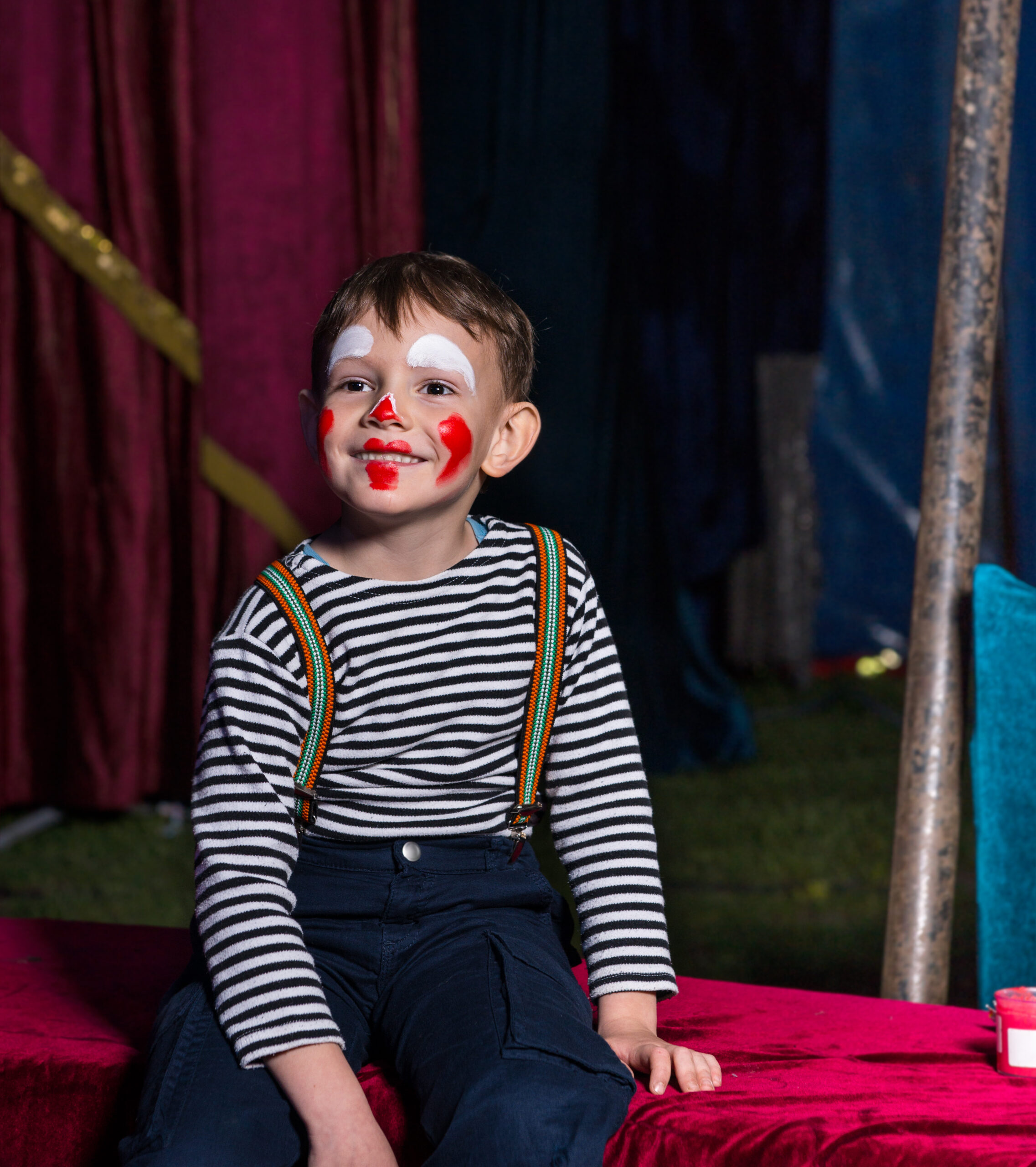 Happy boy with clown make up sitting on a stage
